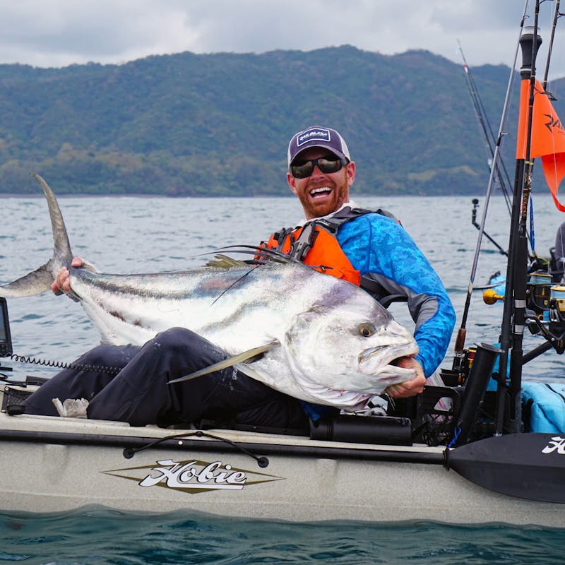 Fisherman sits in kayak with big smile, holding large white fish