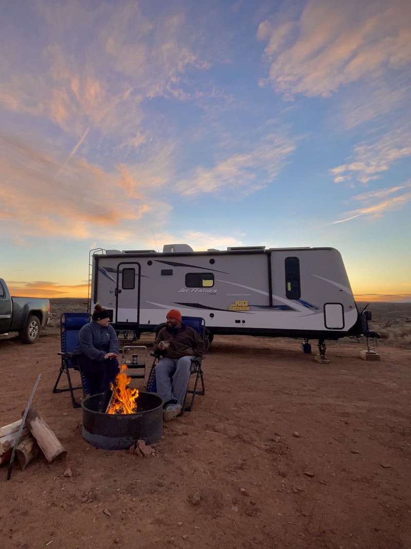 CHRISTINA AND BEN MCMILLAN sit around a fire while boondocking in a desert 