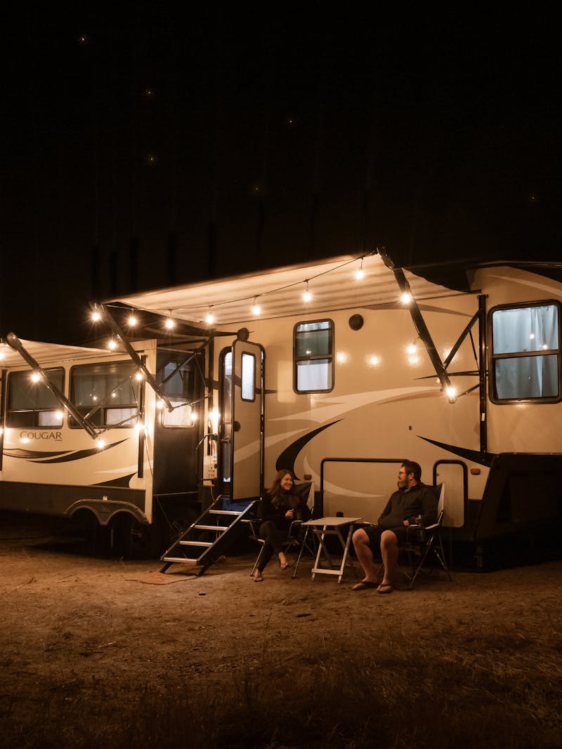 Cindy Scott and her husband sit outside their Keystone Outback at nighttime with string lights on.