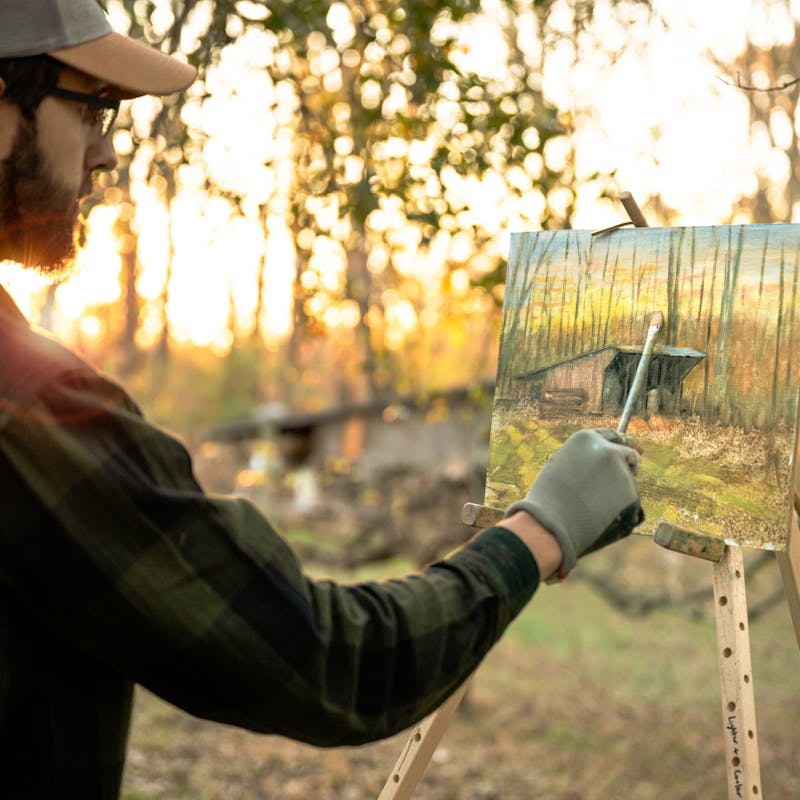 Todd Schabel paints a landscape of an old barn outside as the sun rises.