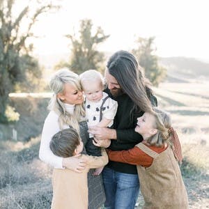 Family portrait of Amber Thrane and her family looking at one another and smiling, with a field in the background.