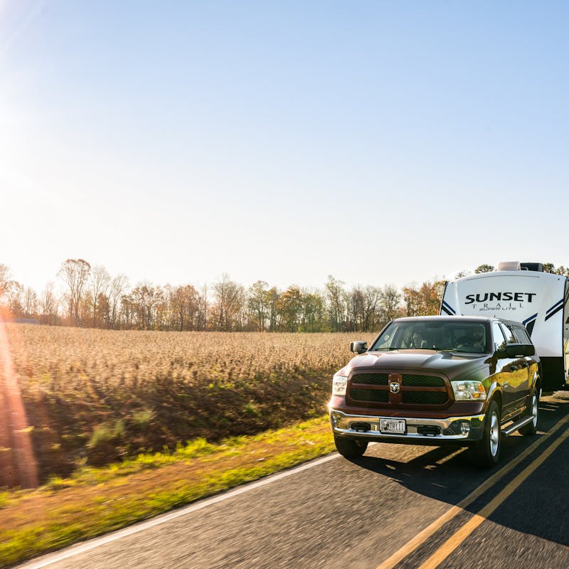Todd & Marcia Schabel driving their Crossroads Sunset Travel Trailer down a road next to a field of crops.