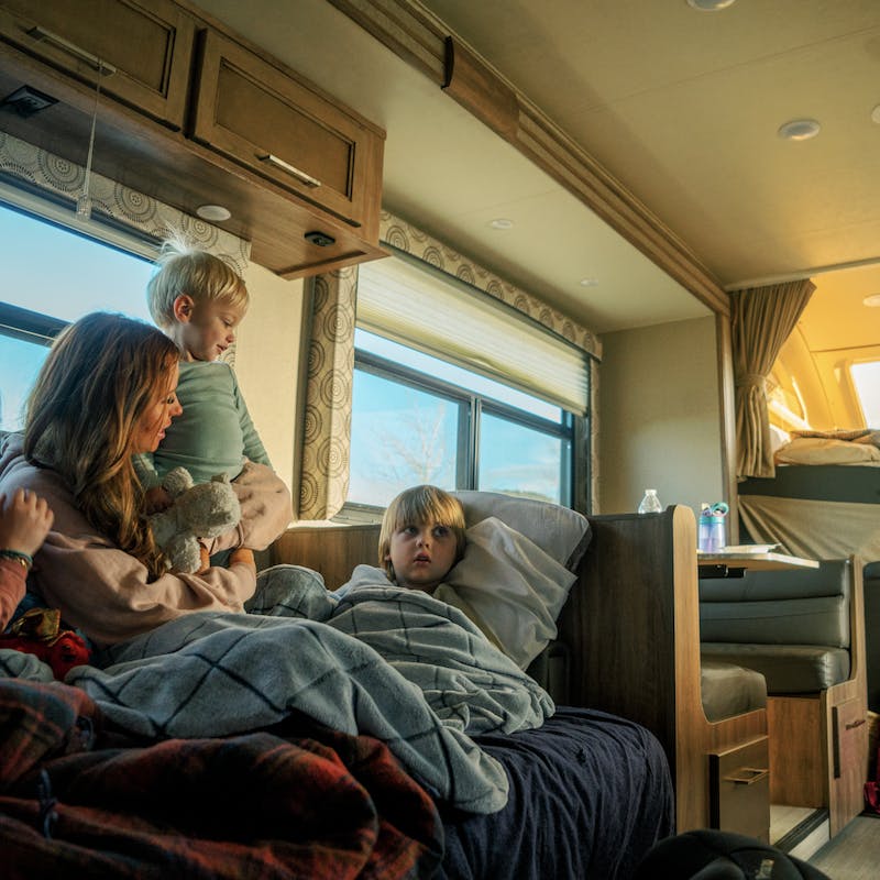 Mother snuggles with three kids inside RV on couch