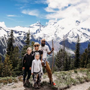 Michelle and Justin Russell with their two kids on a hike with beautiful snow-capped mountain peaks and blue skies