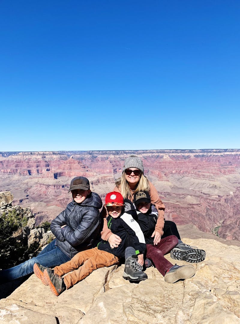 A mom and three boys posed for a picture in front of the Grand Canyon.