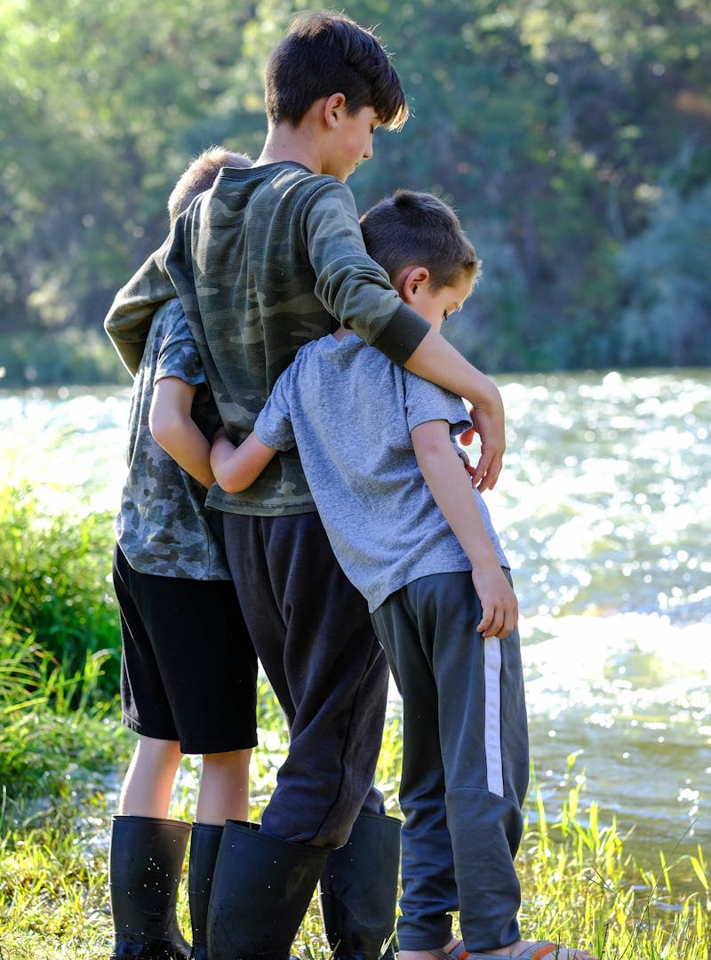 Three young boys stand arm in arm by a river.
