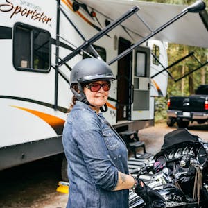 A woman smiles as she sits idle on her motorcycle in front of her toy hauler RV.