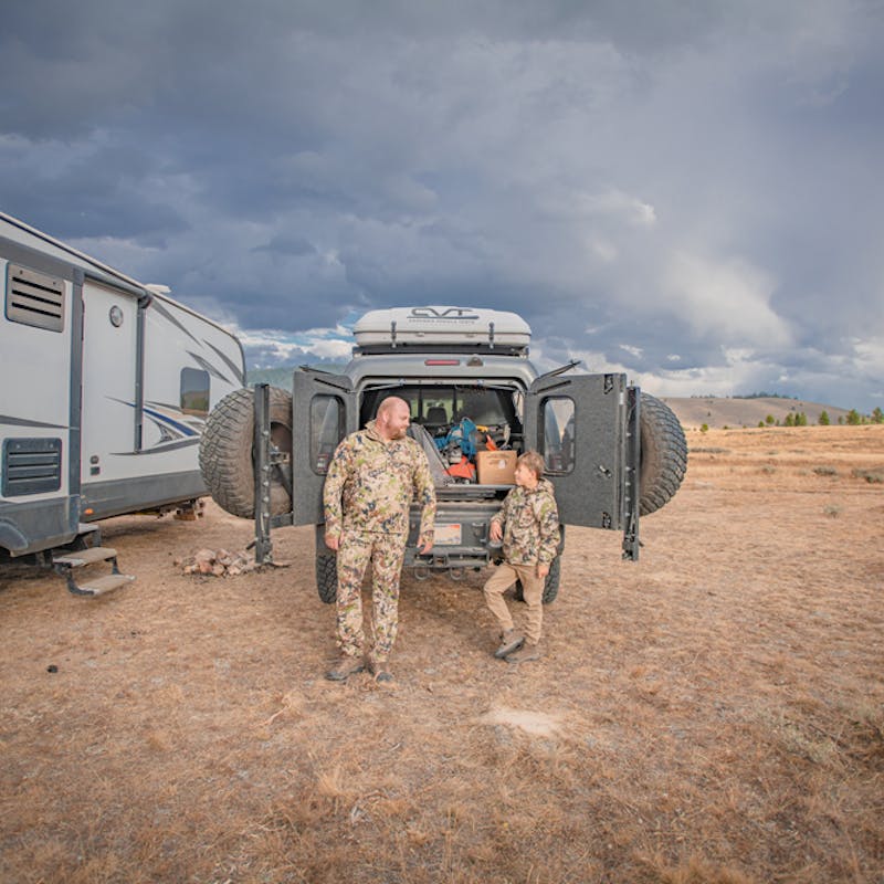 Nate Day and his son in hunting gear stand outside of a truck next to an RV.