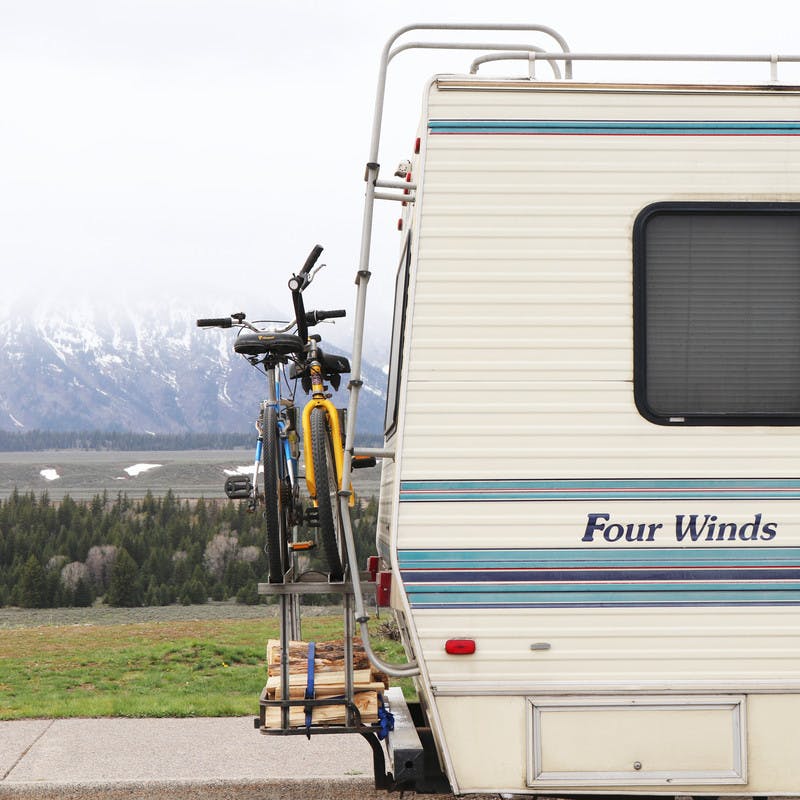 Back of Class C Four Winds motorhome, with two bikes and some firewood strapped to the back, and snowy mountains in the background.