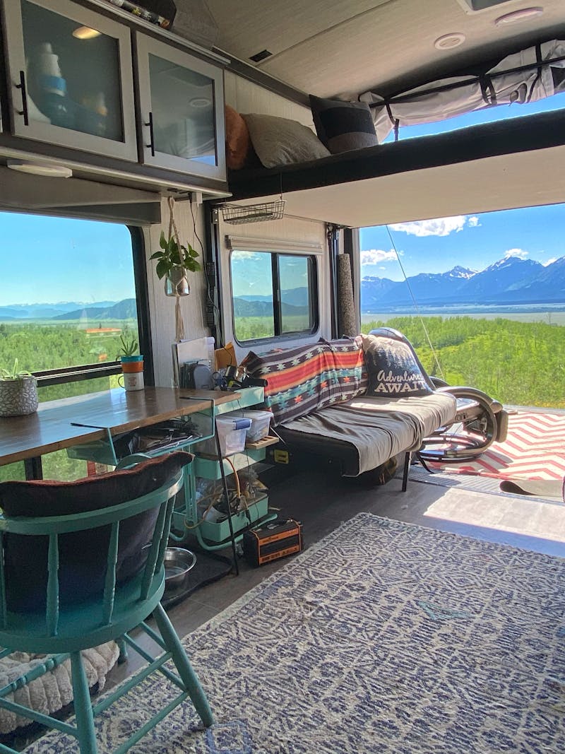 Amy Rekart's Cruiser Stryker toy hauler's back patio opens up to a beautiful mountain scene with lush grass and sunny skies. 