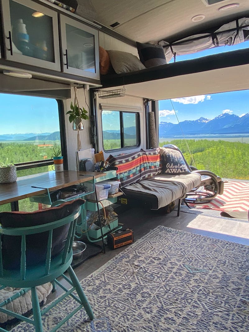 Amy Rekart's Cruiser Stryker toy hauler's back patio opens up to a beautiful mountain scene with lush grass and sunny skies.