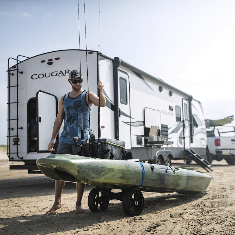 Fisherman stands on beach, in front of Keystone Cougar RV, loading kayak with fishing poles