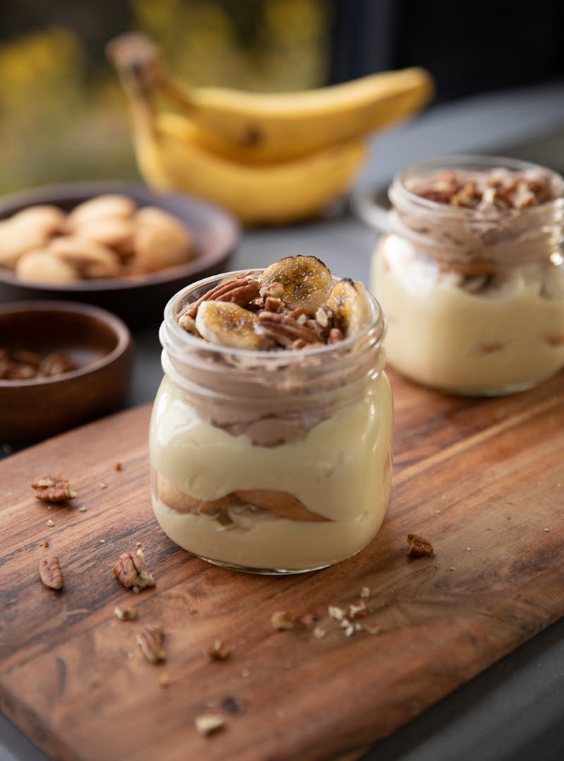 Beautifully layered pudding parfaits in glass jars on top of a wooden cutting board.