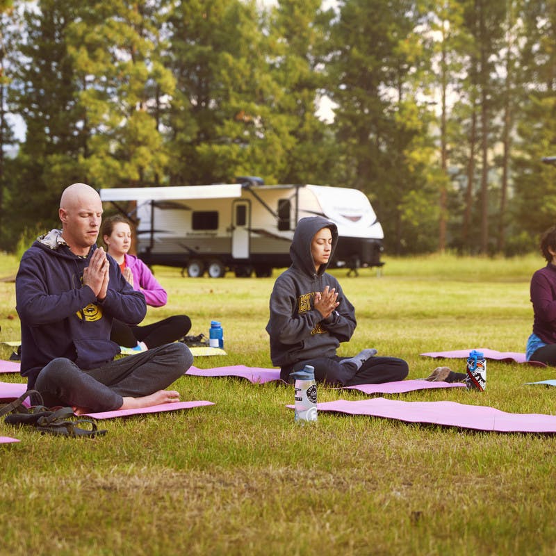 A group of participants sits with their legs folded while practicing yoga outside of the travel trailers where they sleep.