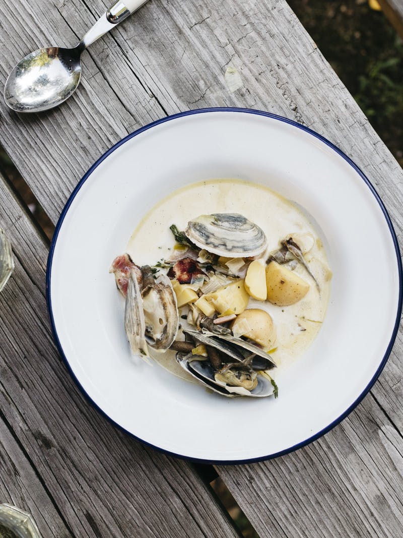 A bowl of freshly made clam chowder on a rustic picnic table outside.