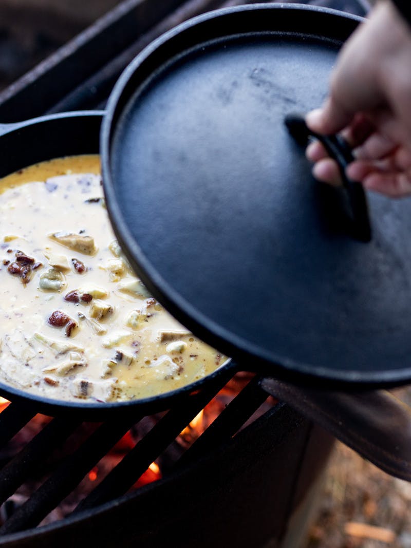 Campfire bacon artichoke frittata being cooked over a fire in a pan.