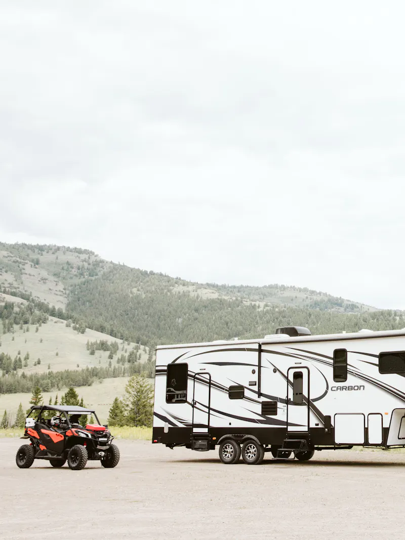 A fifth wheel toy hauler RV parked next to a side by side.