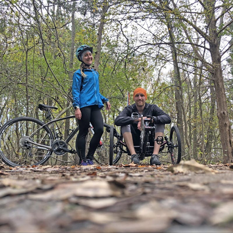 A woman and her husband in a forest with their mountain bikes.