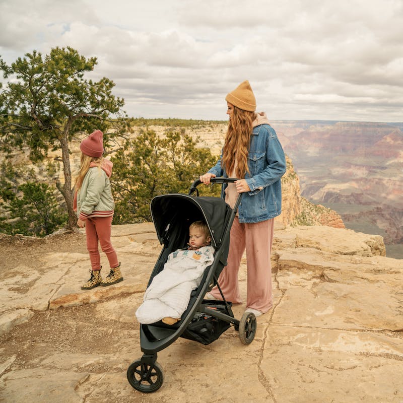 Women in yellow hat pushes stroller with little girl standing next to her on edge near Grand Canyon