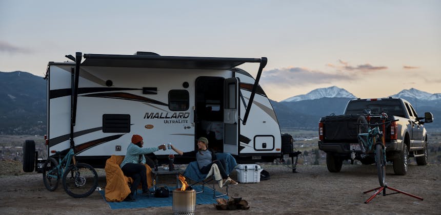 Britt Greer and Brooke Goudy cheers by a fire outside of a Mallard travel trailer