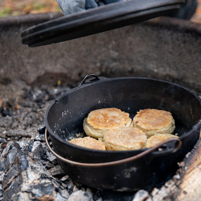 Biscuits in a dutch oven cooking over coals and getting toasty and golden brown.