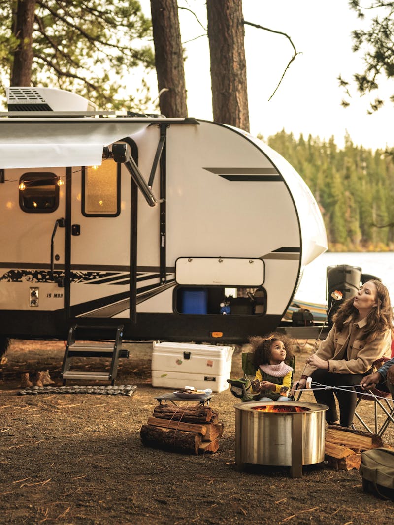 A family makes smores outside of a travel trailer