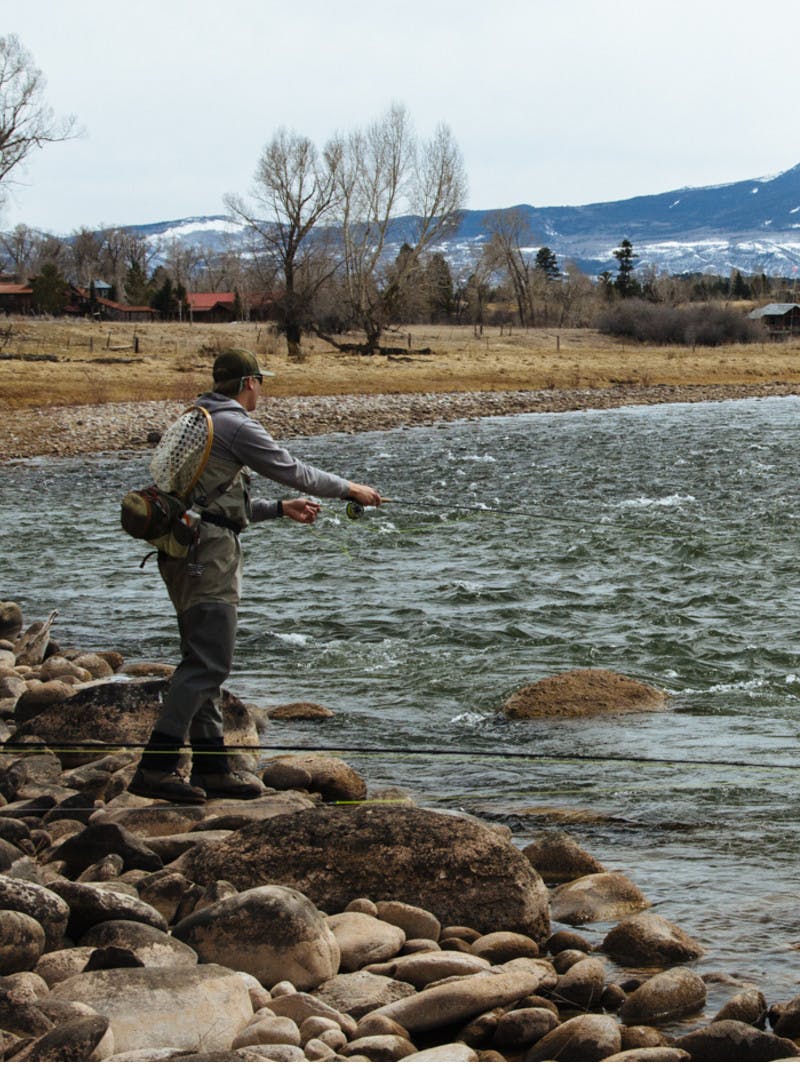 A man fishing on a lake at the base of a mountain.
