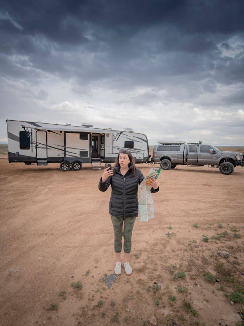 Chelsea Day holding up a map and a phone in front of her travel trailer RV