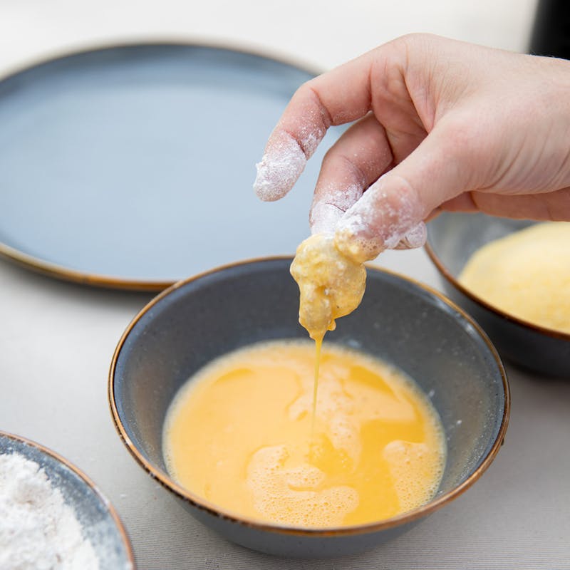 Coating shrimp in batter before frying.