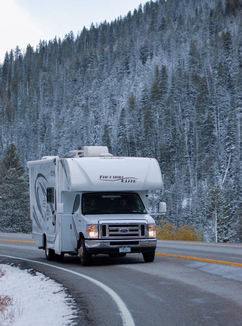 Class C RV drives along windy, snowy mountain road