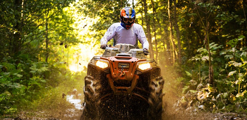 A man ATVs through a muddy forest trail.
