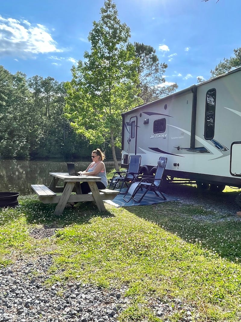 Christina McMIllan working on her laptop outside of her RV at a lovely campsite