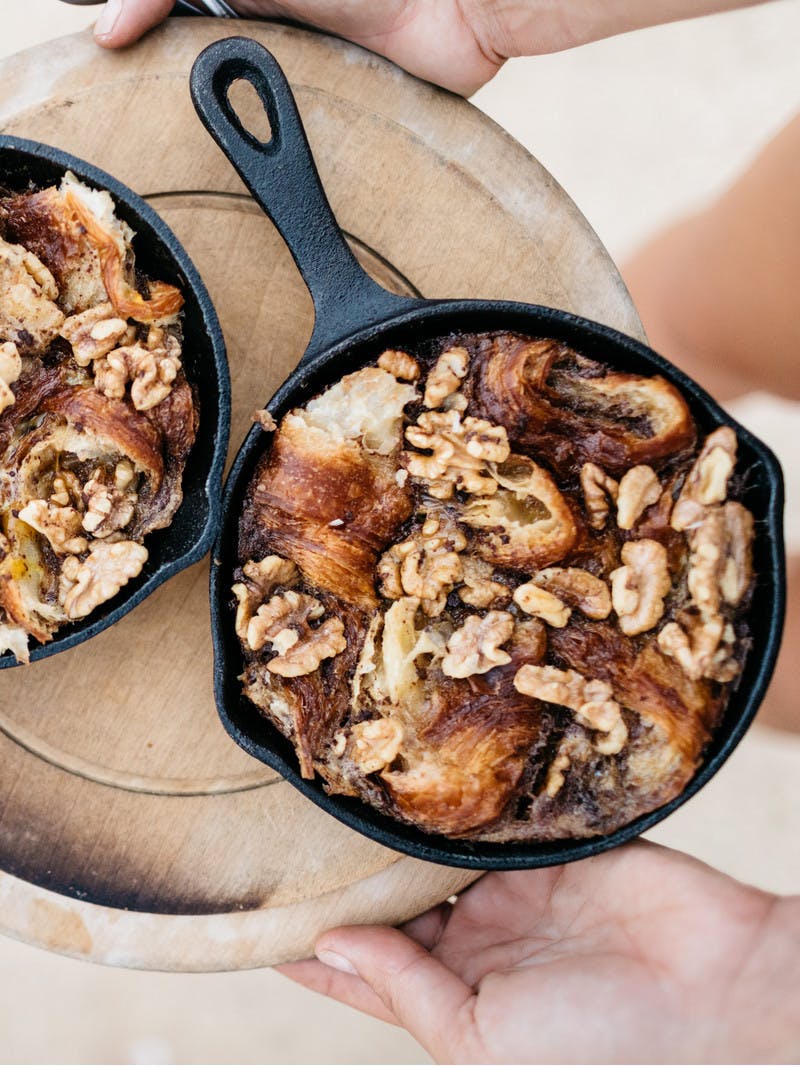 Two mini cast iron skillets on a tray, holding warm caramelized maple walnut croissant pudding. 