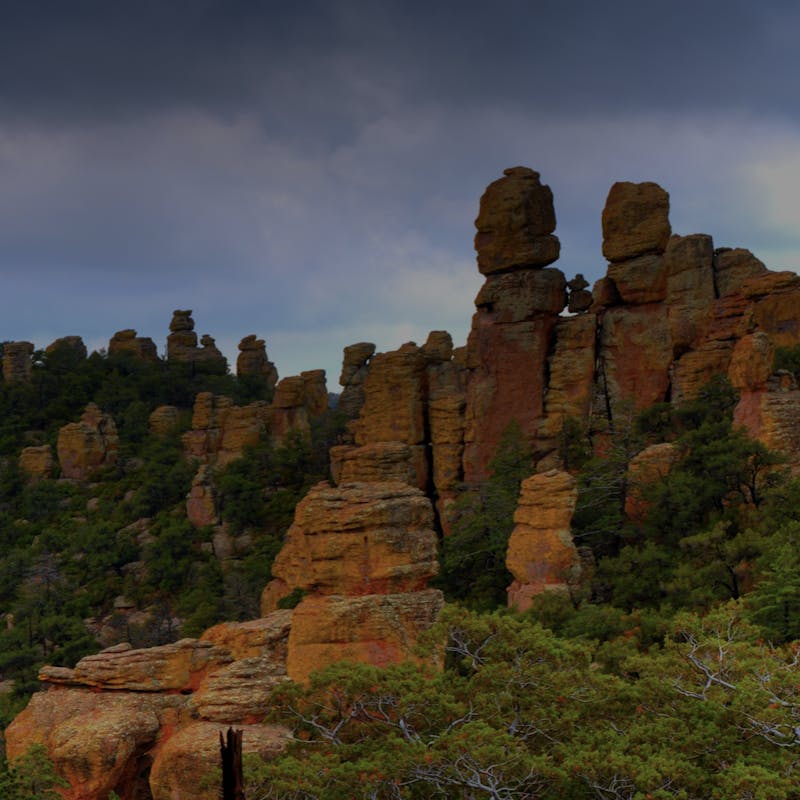 Tall, red Chiricahua mountains stacked on top of each other, surrounded by green trees