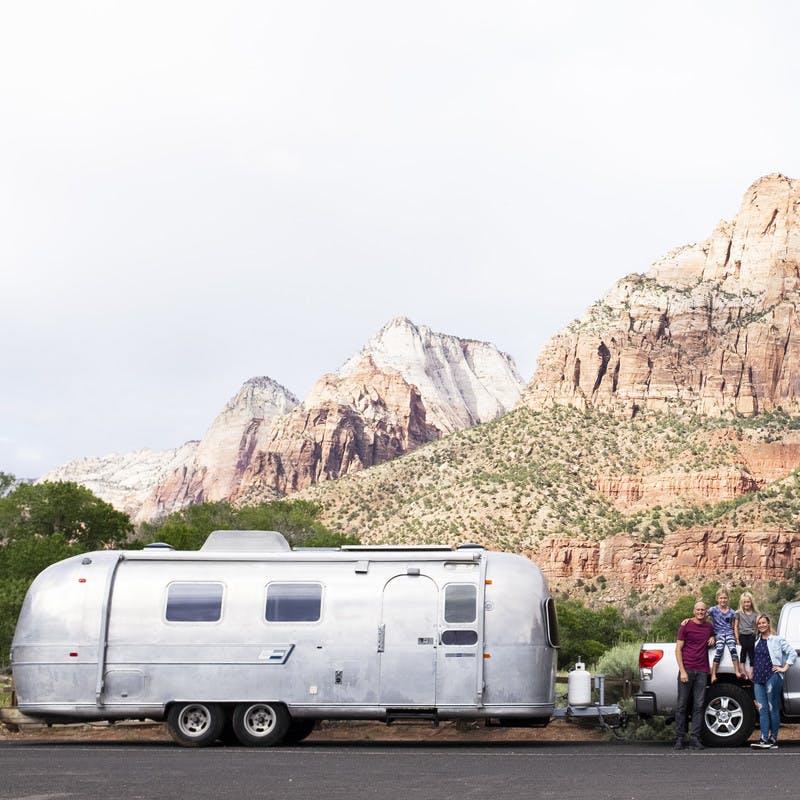 Family standing in front of truck and Airstream travel trailer. Background includes large rock formations.