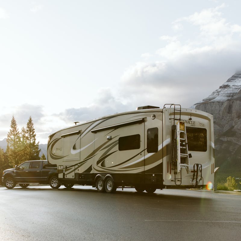 A shot of a truck pulling an RV with mountains in the background and golden light rising on the left.