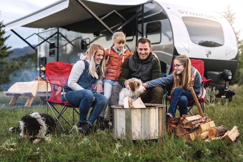 a family sits around a campfire with two dogs in front of a venture stratus rv
