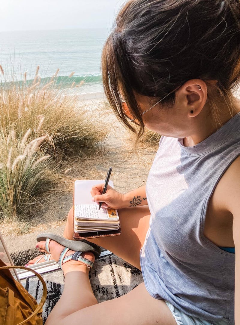 Jess Lawson journaling while sitting in the doorway of her class B RV, a Thor Motor Coach Tellaro.
