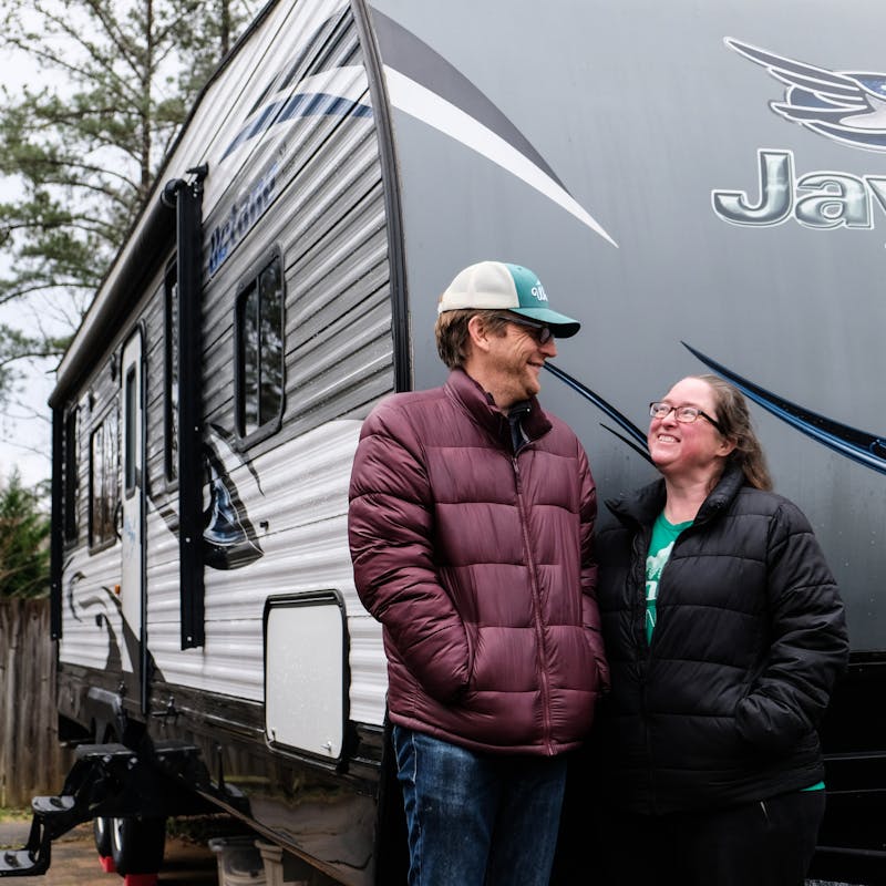 Gretchen Holcomb and her husband smile at each other while they stand in front of their Jayco Octane toy hauler.