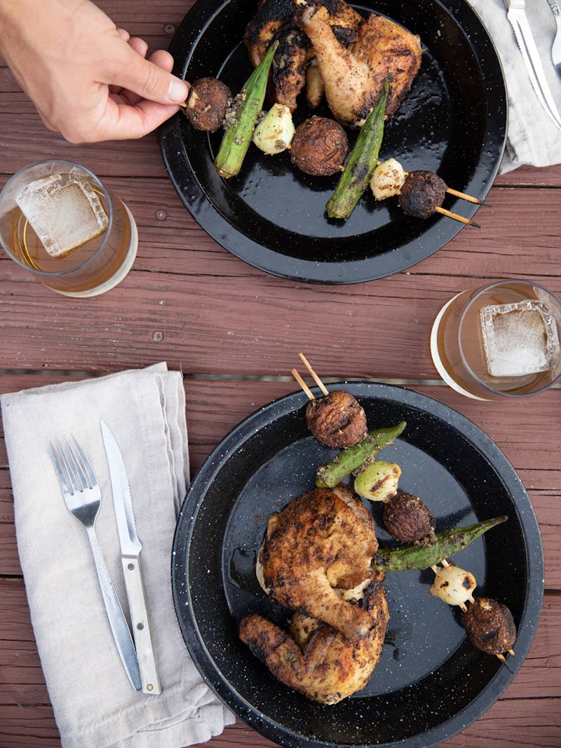 A top down view of two plates holding cooked Cornish hens and okra kabobs. 