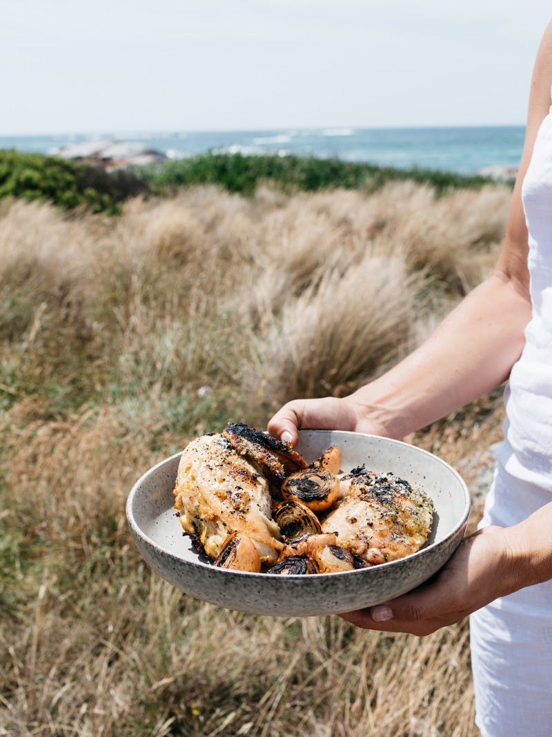 Close up of hands holding a bowl of cooked chicken and grilled vegetables.