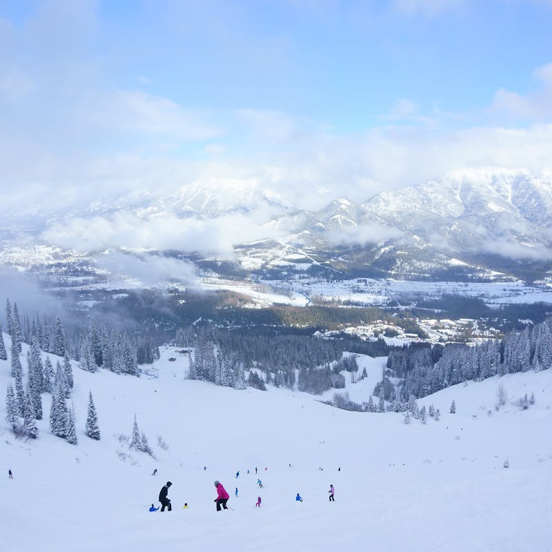 View down a ski lift to snowy slopes with pine trees and cloudy mountains in the background