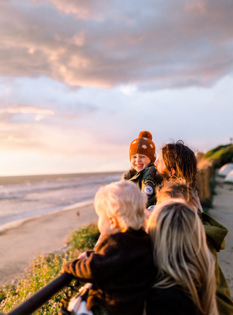 Amber Thrane and her family watching the sun set by a fence, with the beach & ocean in the background.