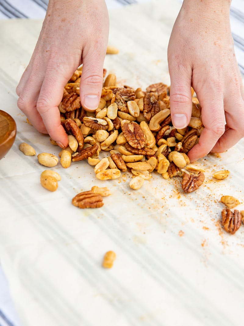 Hands mixing nuts together with cajun spices on parchment paper. 