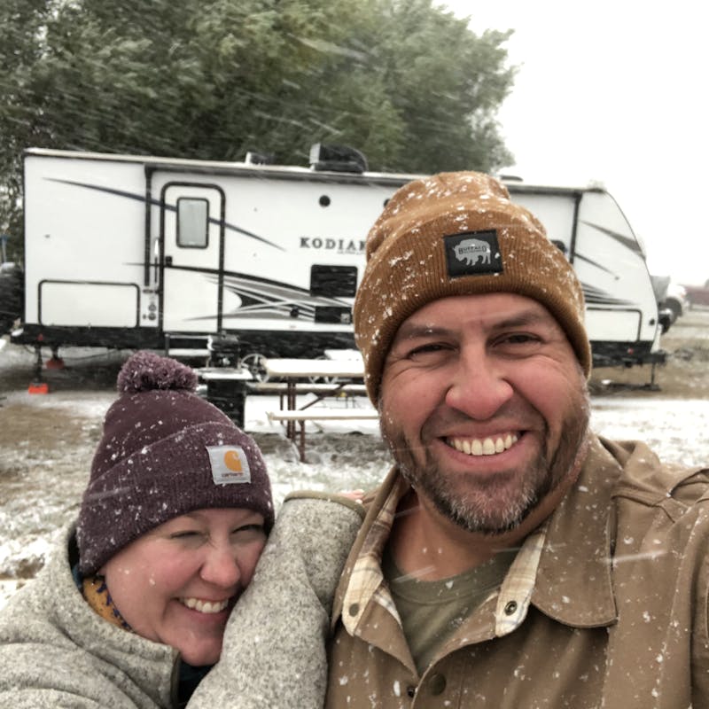Abby Booth and her husband smile in the snow for a selfie in front of their Dutchmen Kodiak travel trailer.
