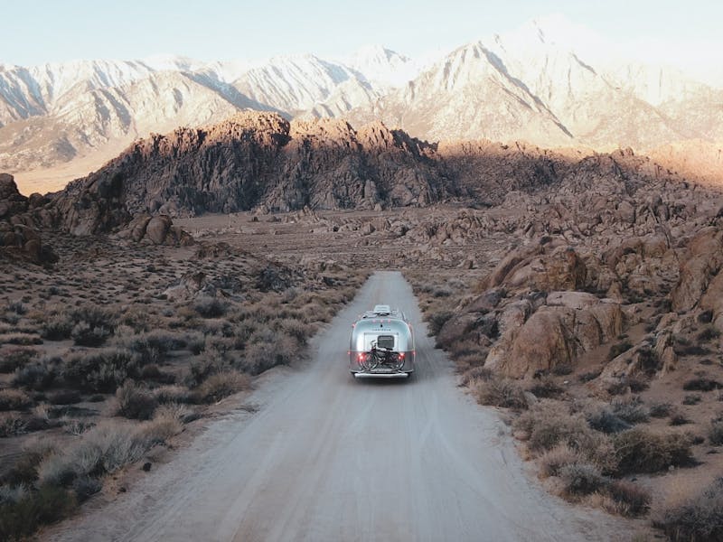 Airstream on dirt road surrounded by desert driving towards mountains