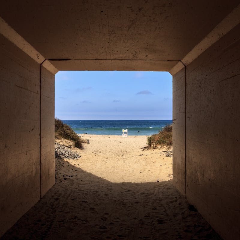 View inside a tunnel looking out at sandy beach, blue ocean and blue sky