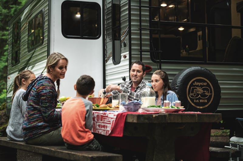 A family sitting at a picnic table next to a jayco RV travel trailer