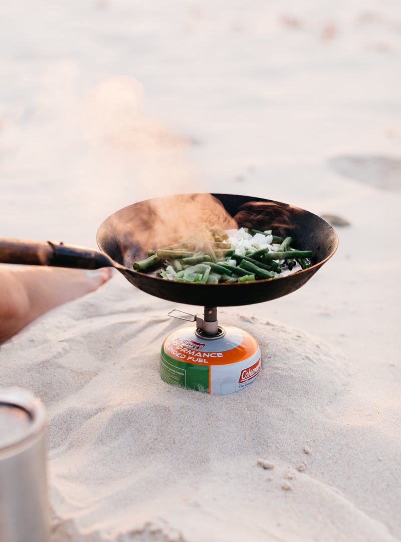 Green beans and a leek cooking in a cast iron skillet over a flame.