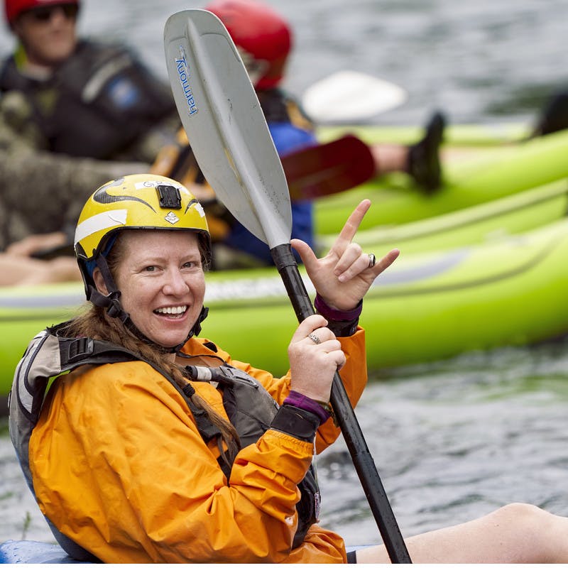 A participant wades in the water in her kayak while throwing up a "rock and roll" sign.